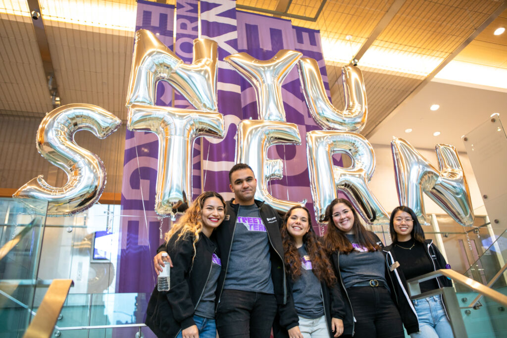 Five NYU Stern students posing in front of balloons