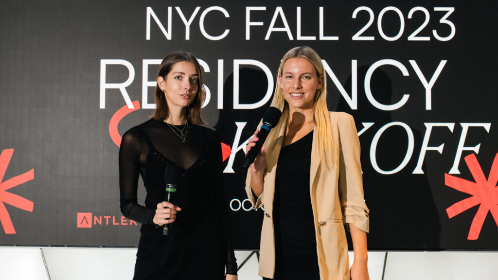 Two women standing in front of a wall with text on it reading "NYU Fall 2023 - Residency Kick Off"